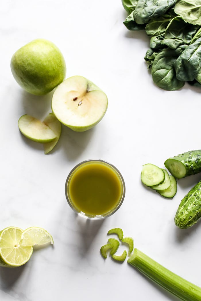 A refreshing top view of fresh green juice surrounded by fruits and vegetables on a white background.